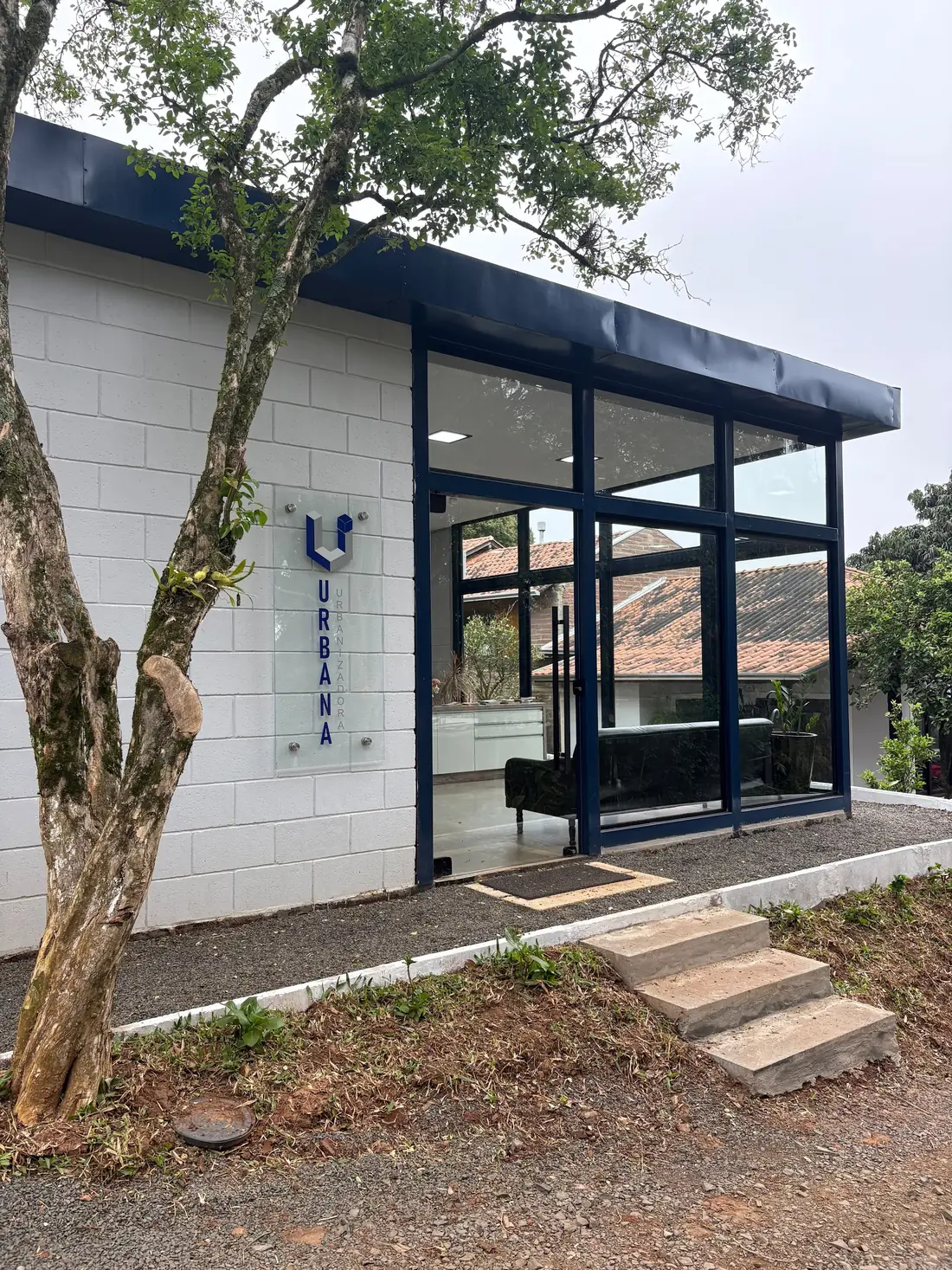 Fachada do escritório da Urbana: parede de bloco branco, esquadrias azul-marinho e a placa com o logo